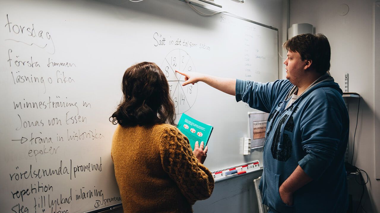 Två personer står framför en whiteboard och diskuterar kring ett matematikproblem. Foto. 