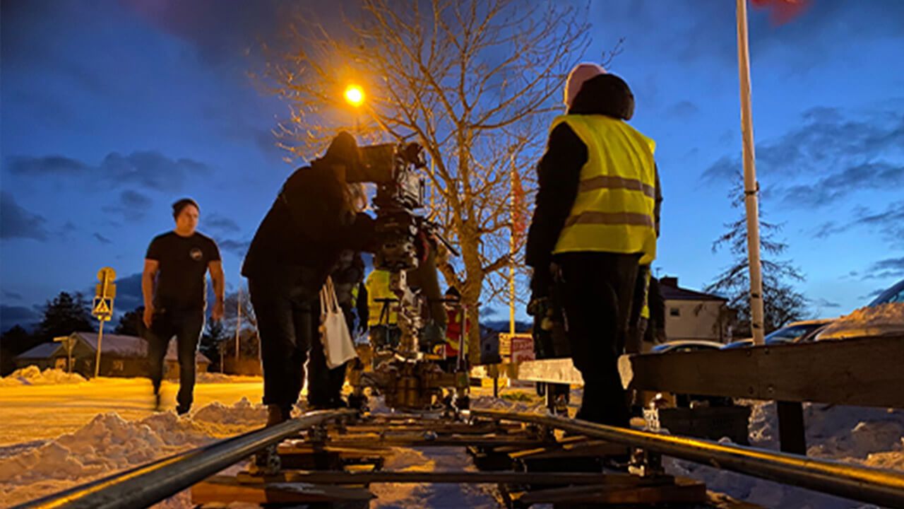 Ett filmteam står utomhus i snön runt en filmkamera på räls. Foto. 