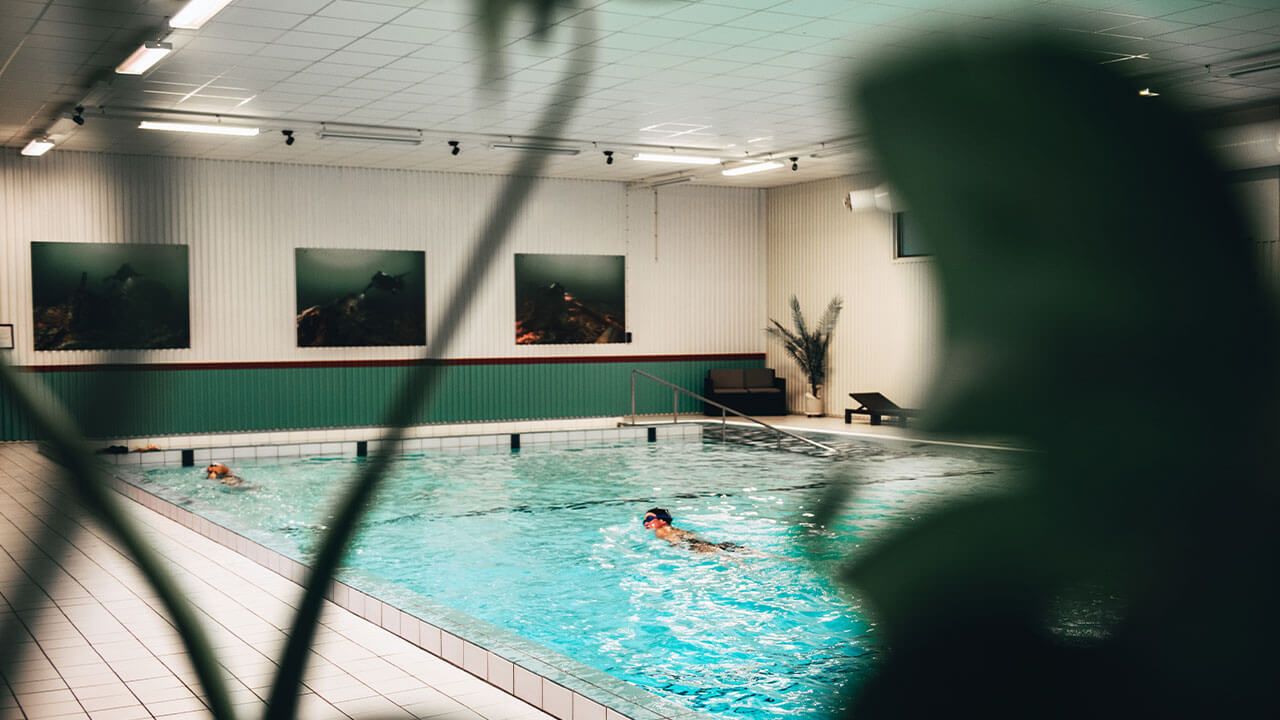 Inomhusbassäng med en person som simmar. Foto. 